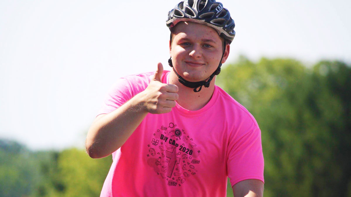 Aiden wearing a pink shirt and a bike helmet giving a thumbs-up